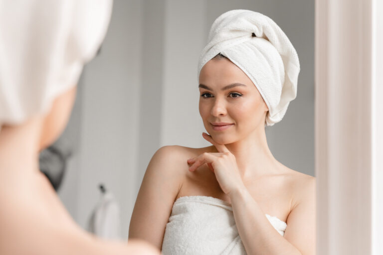 Caucasian white woman with clean young clear skin in spa bath towel looking at the mirror. Beauty treatment, body and hair care. Girl after taking bath shower at home